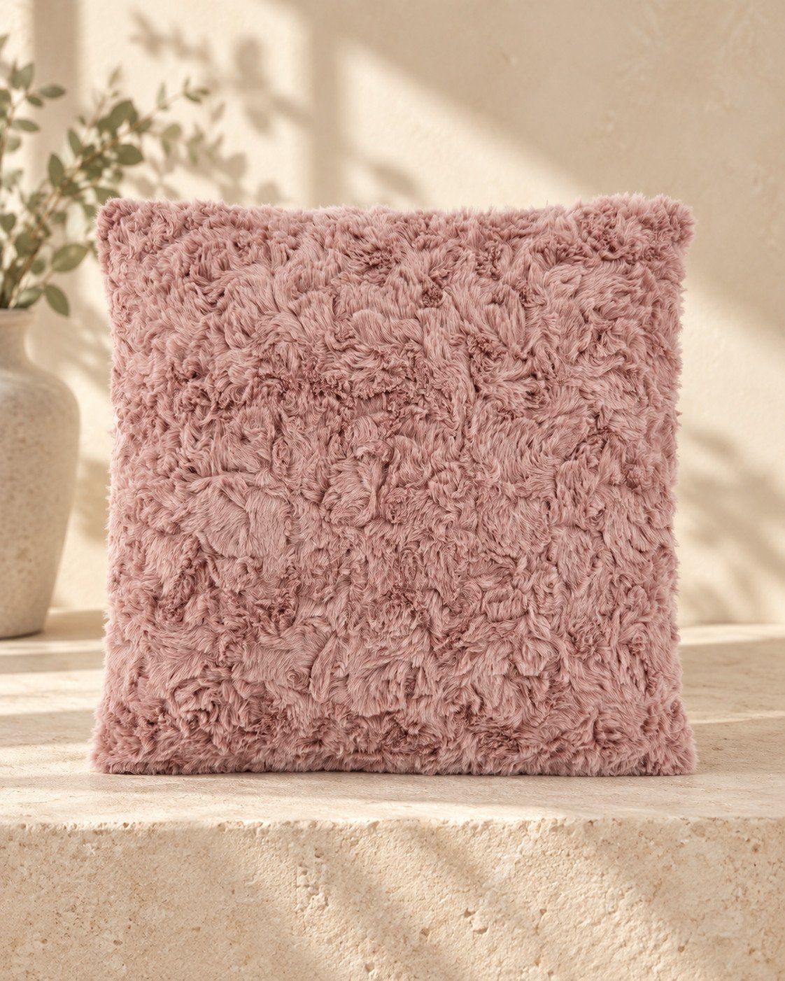 Cojín de pelo efecto aguas en rosa sobre un banco de piedra