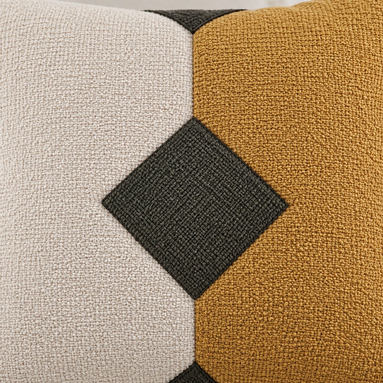 Detalle del rombo verde entre los tejidos beige y mostaza del cojín tricolor